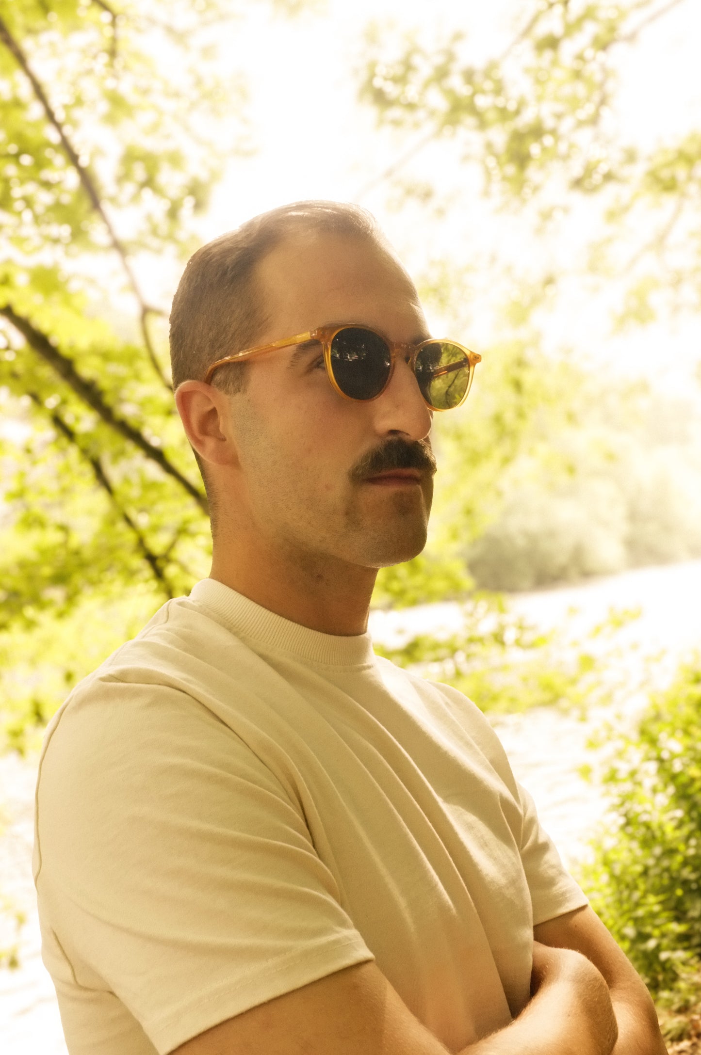 Man wearing sunglasses and a beige shirt in a forest setting