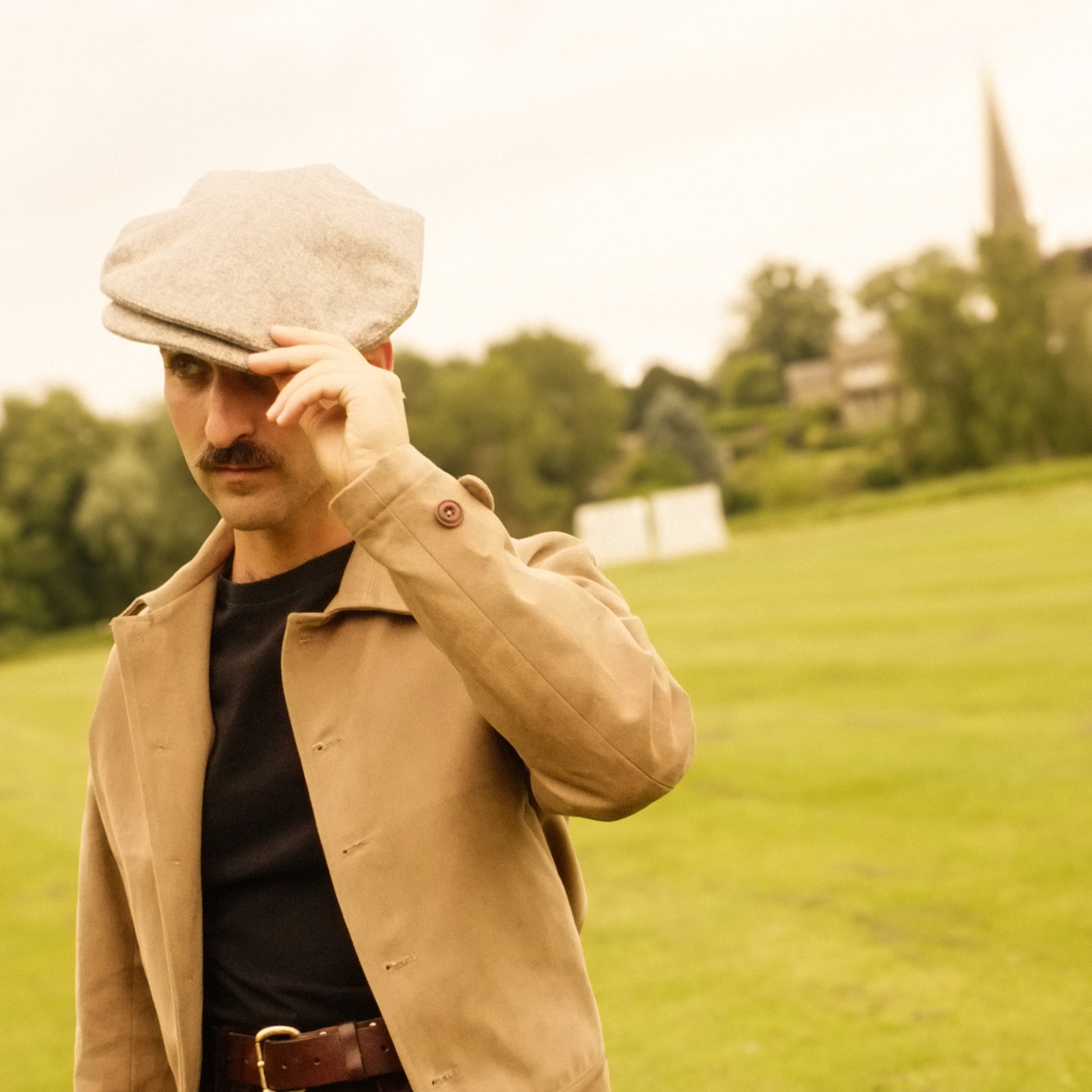 Man in a beige jacket and cap standing in a grassy field.